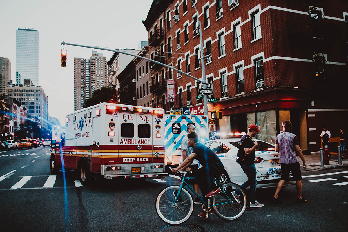 City traffic with ambulance, bike rider, and pedestrians at cross walk