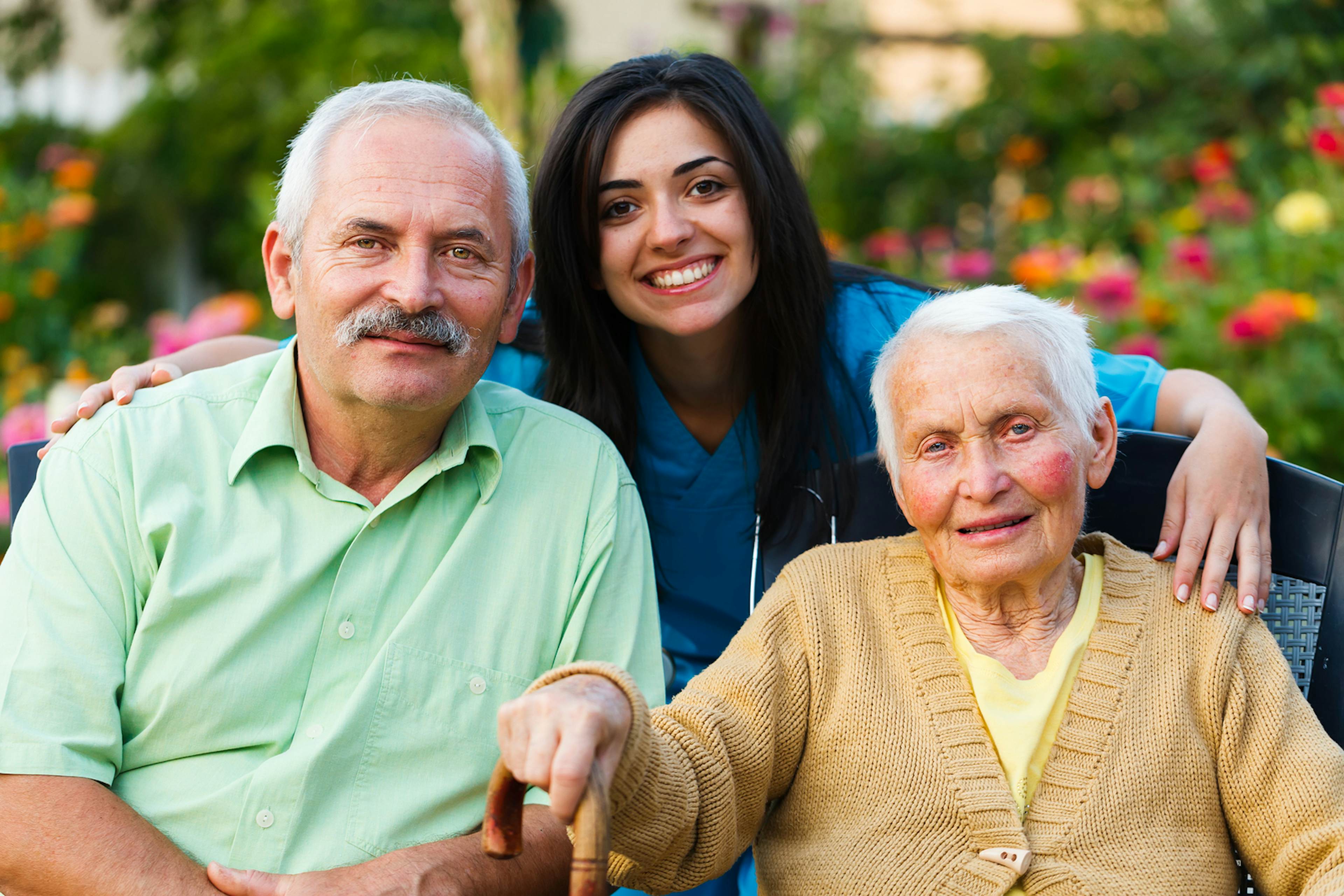 elderly man and women sitting down with a nurse posing for a photo
