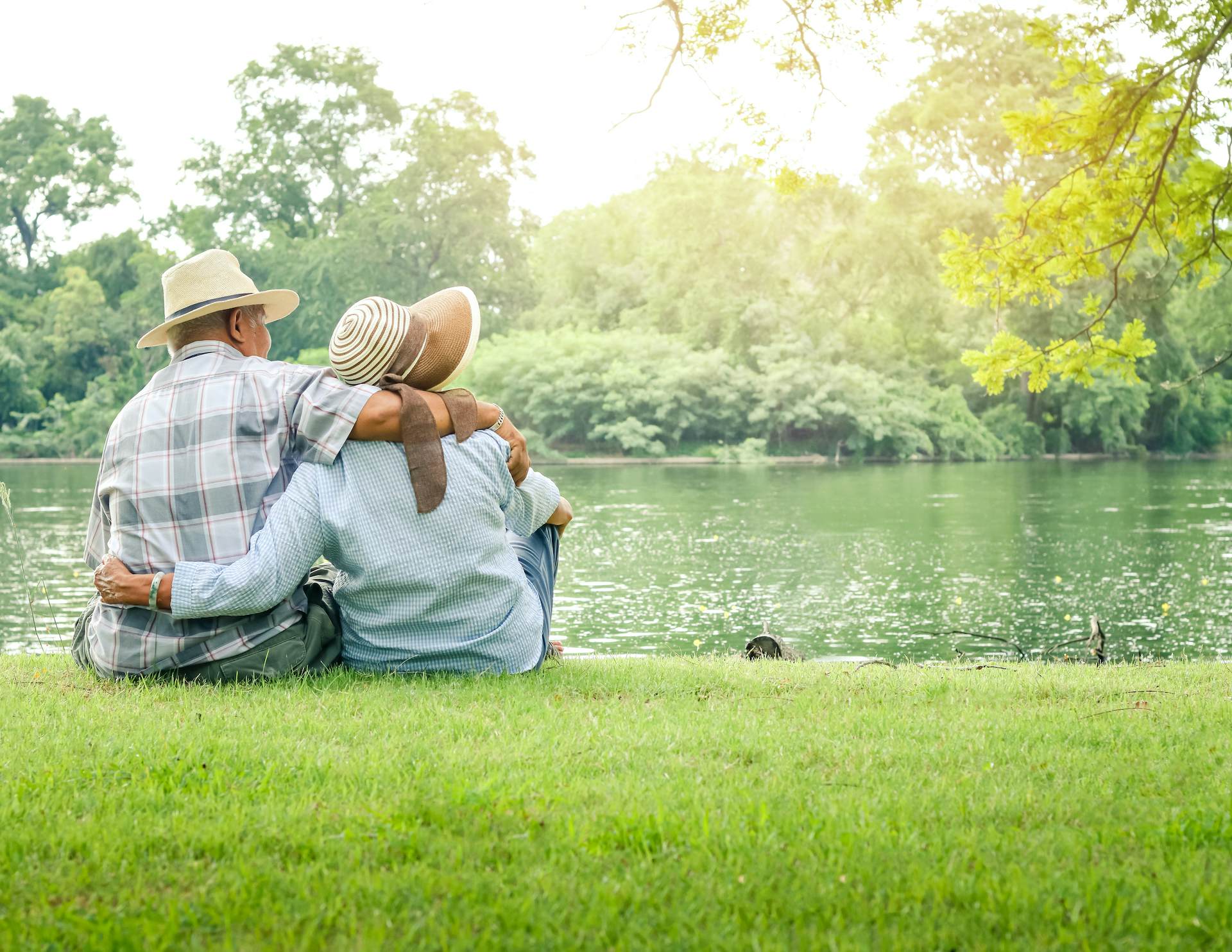 man and woman sitting in the grass embracing each other in front of the lake