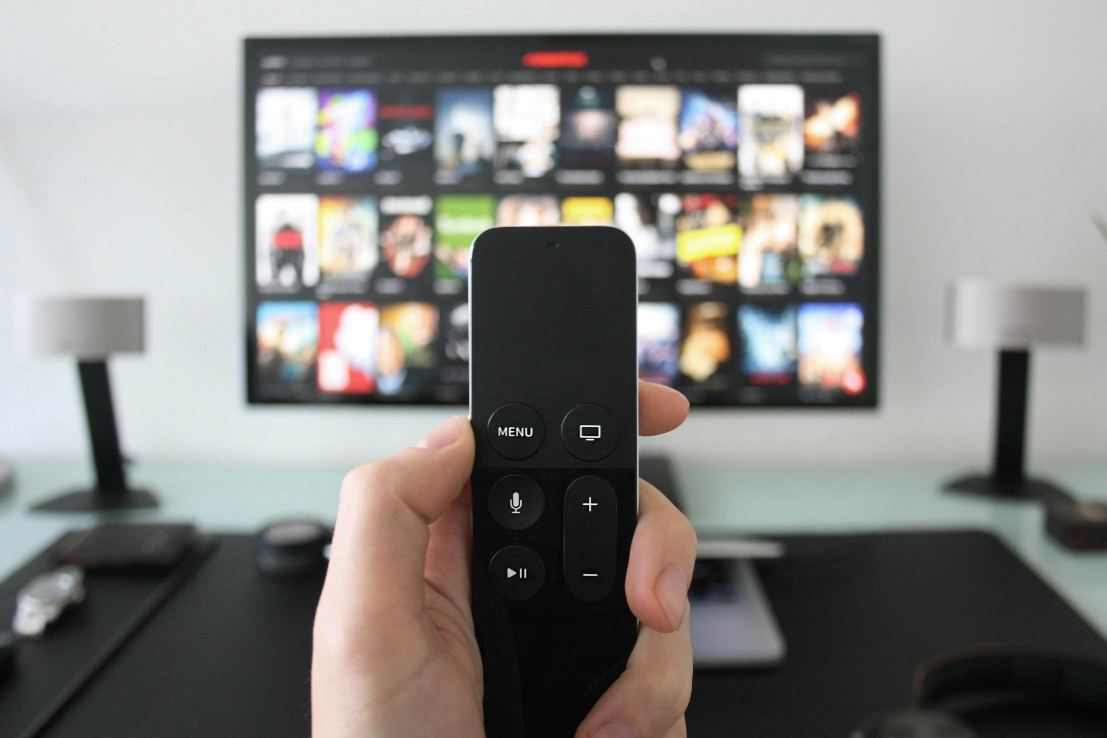 hand holding apple tv remote in front of tv screen