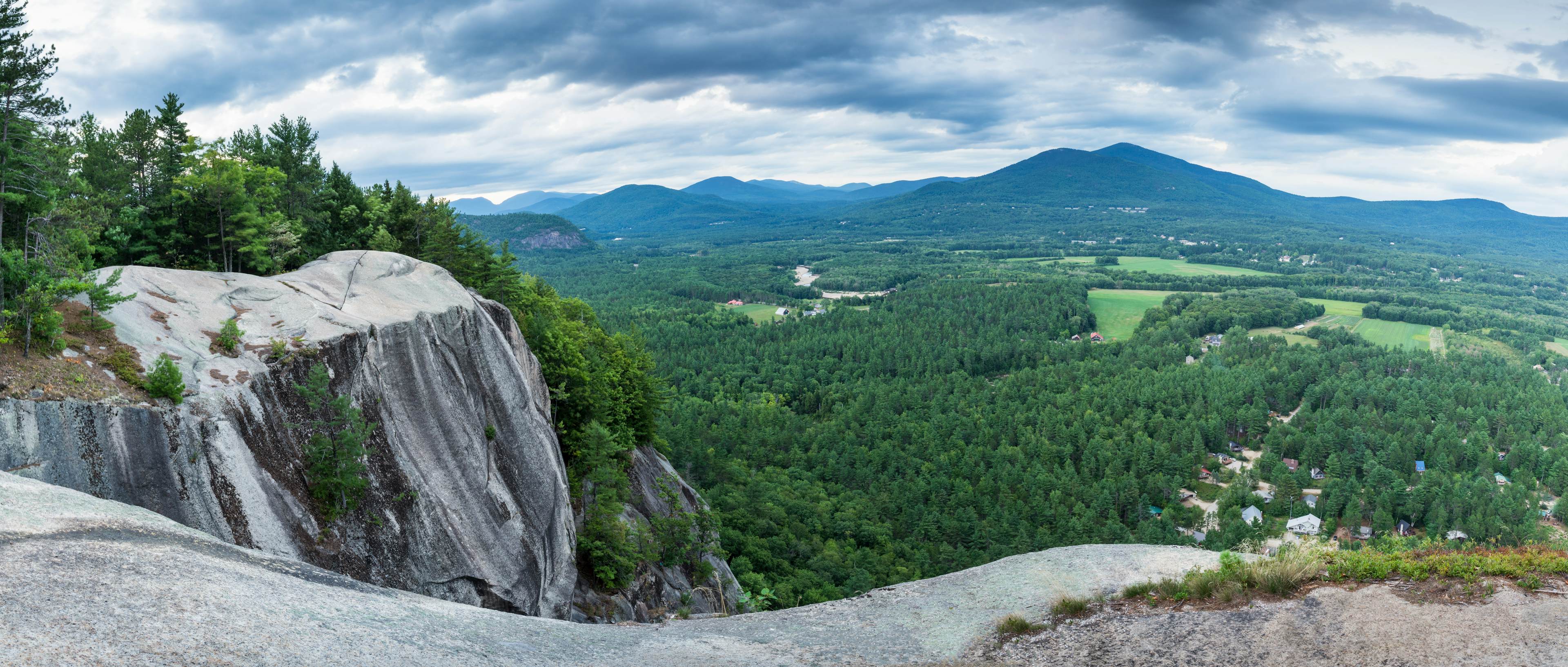 NH rocky cliff, forest below, mountains in distance