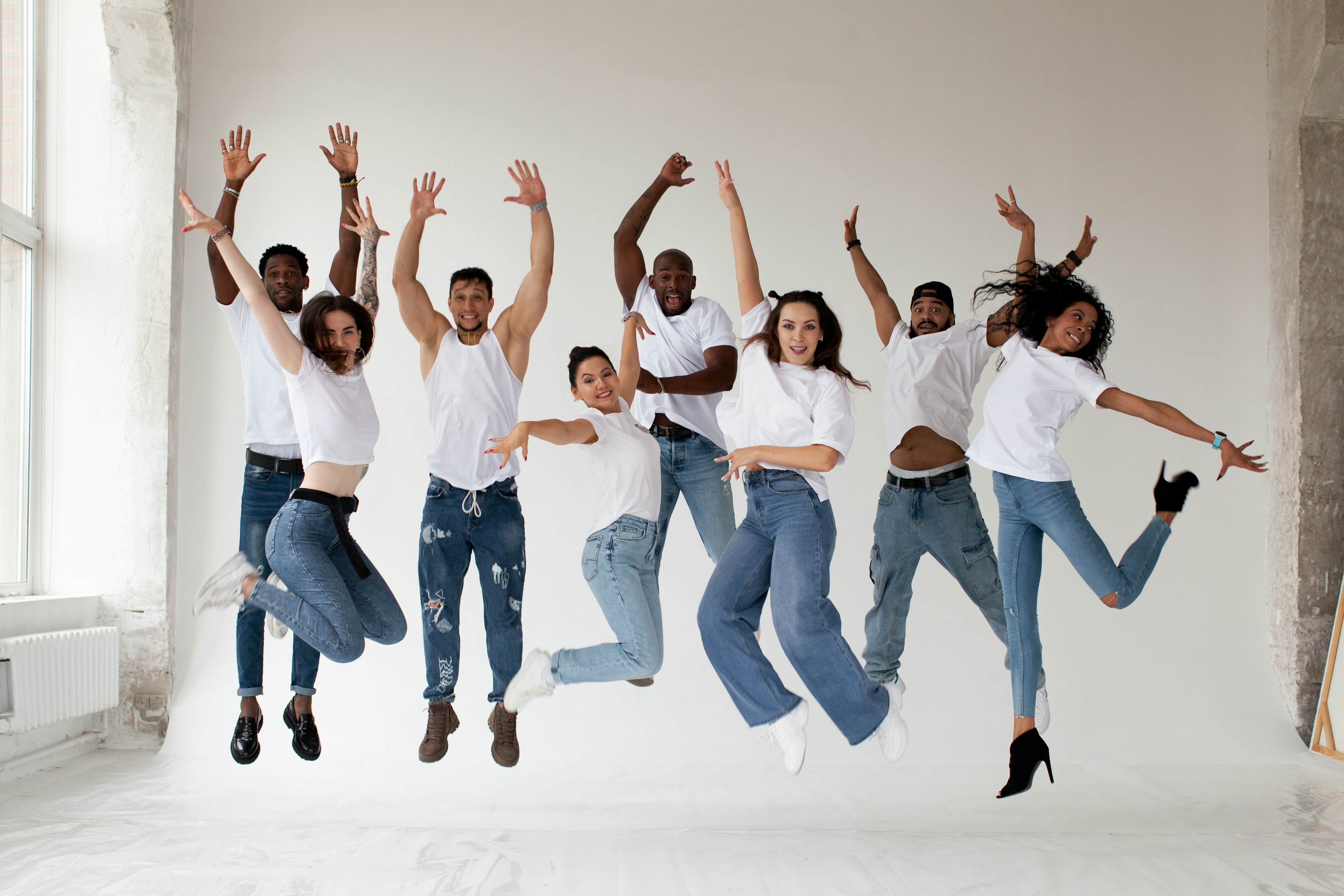 Group of people wearing white shirts and jeans all jump simultaneously