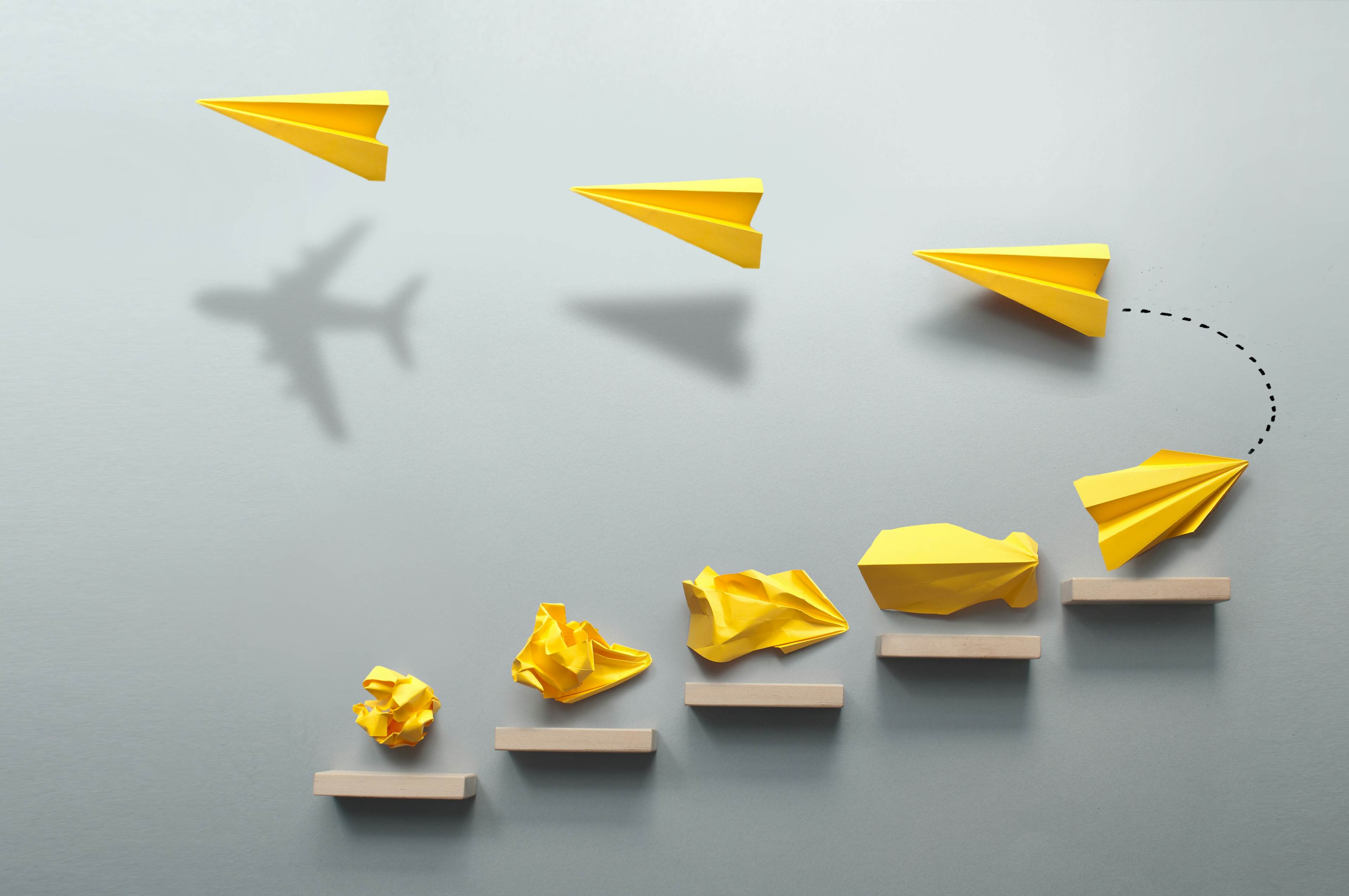 Yellow paper planes evolve from crumpled forms to flight, symbolizing progress, innovation, and transformation.