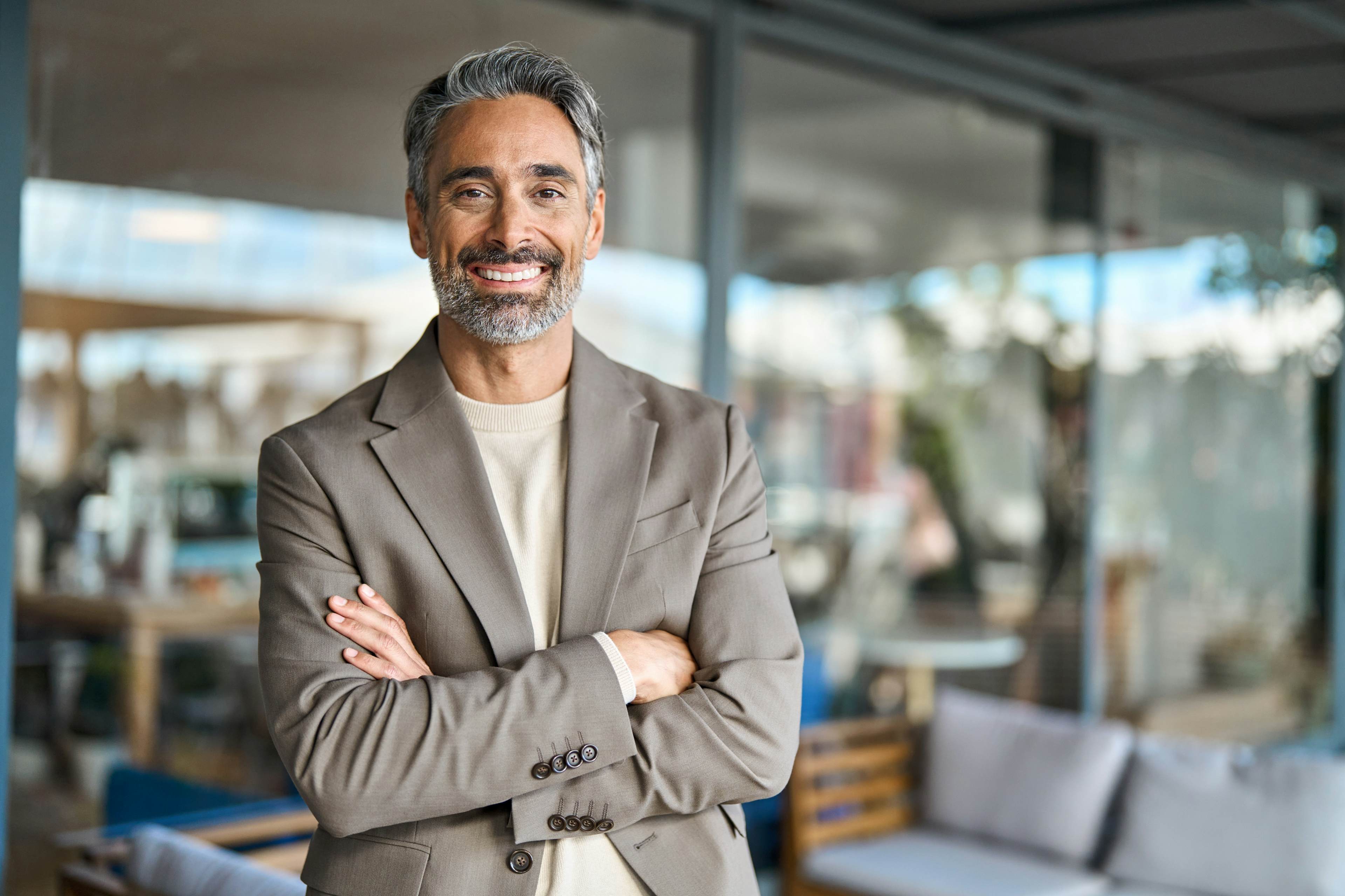 Smiling man in tan blazer with arms crossed, standing outside