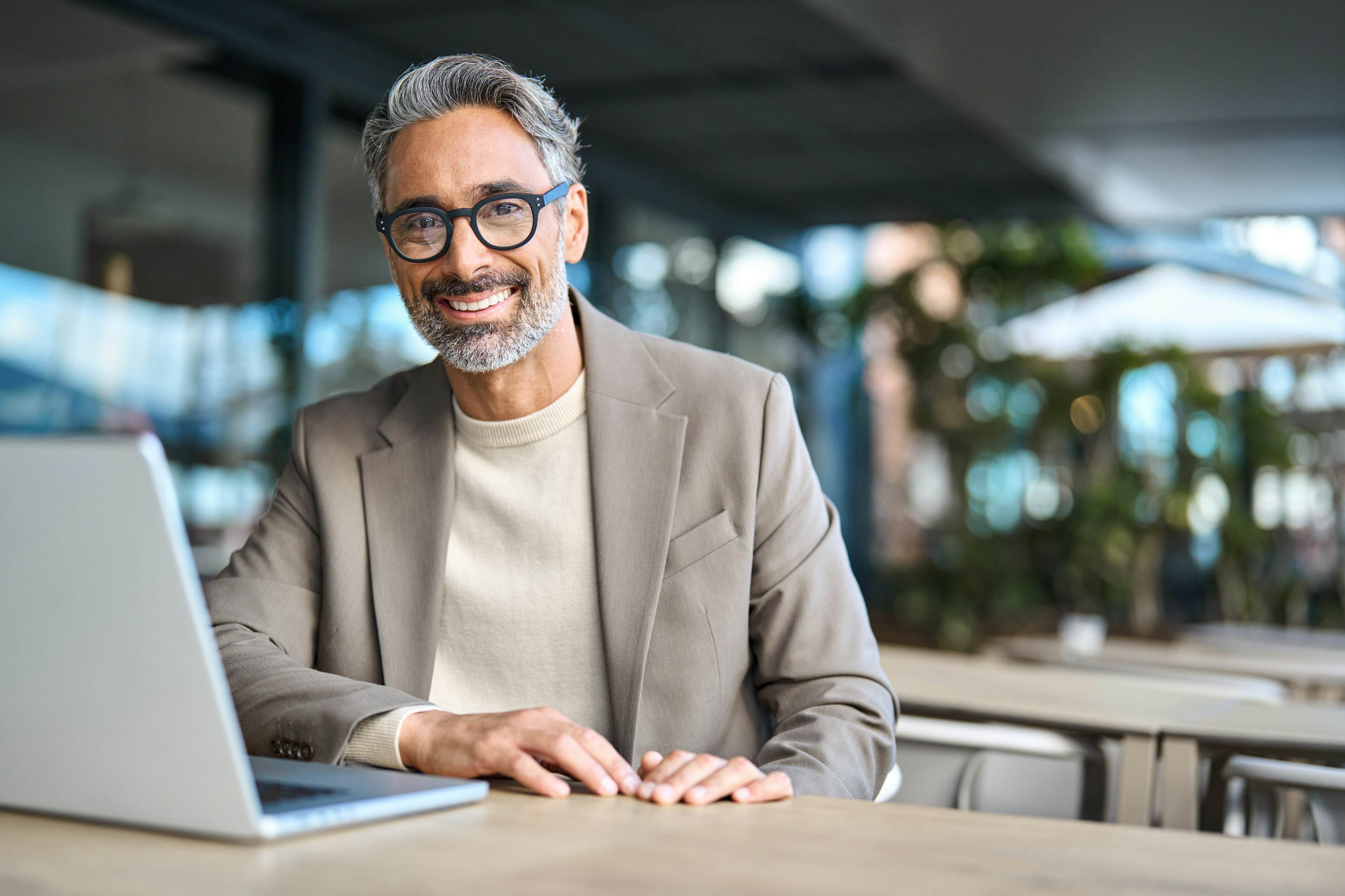 Man smiling at desk wearing glasses and laptop out