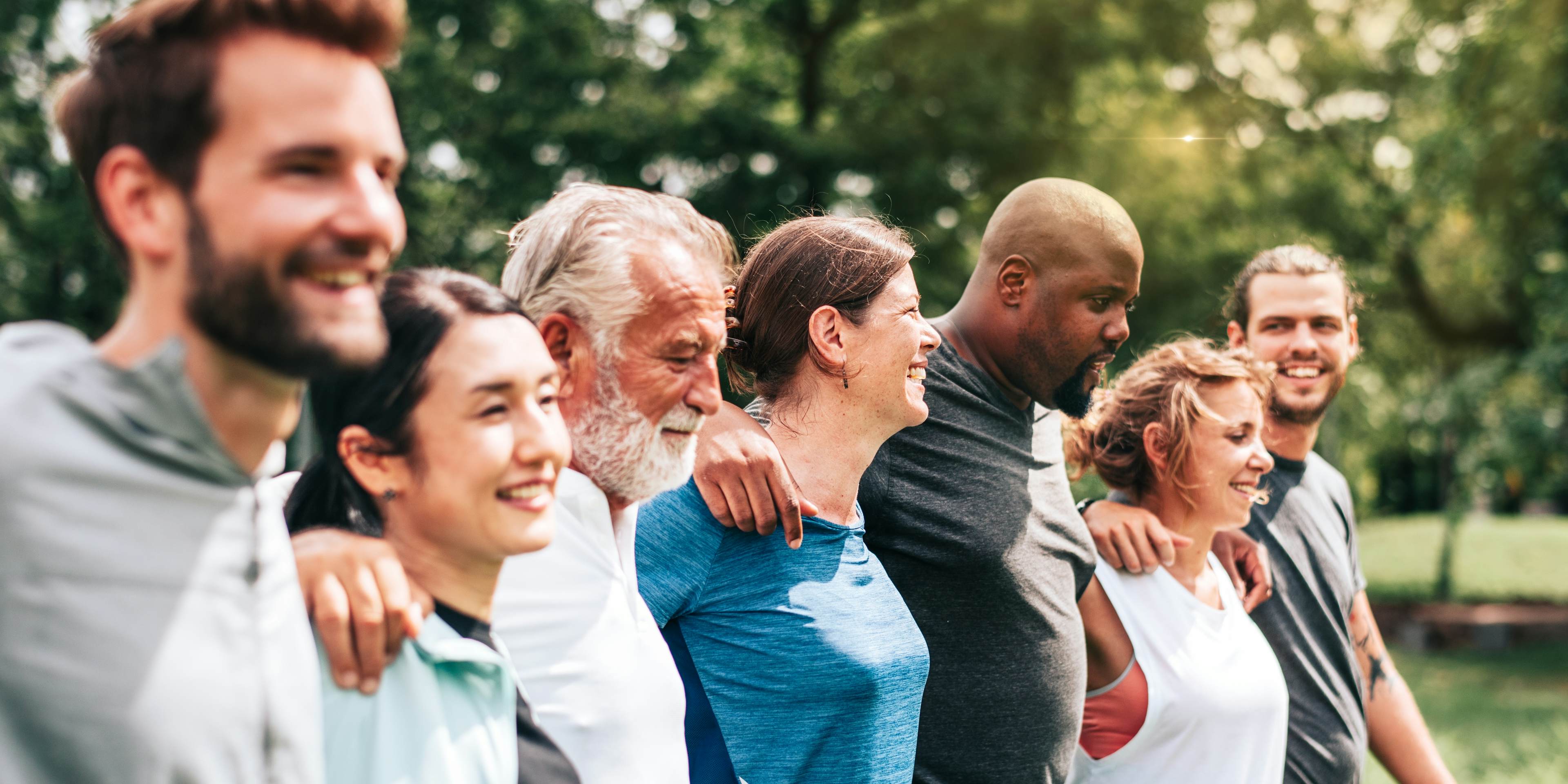 Diverse group of sporty people standing together outdoors, smiling warmly.